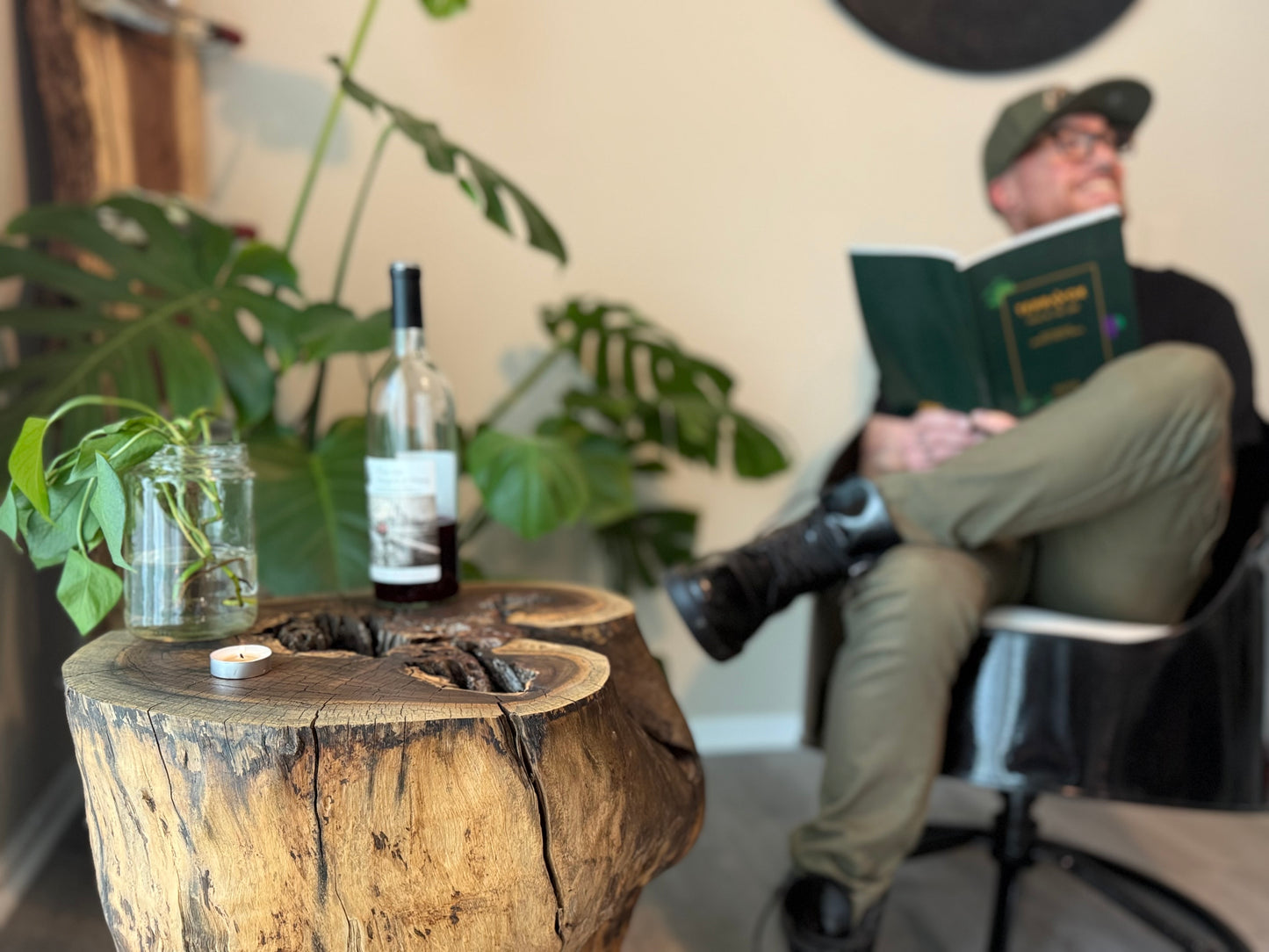 Person reading a book with a bottle of wine on a wooden table in a cozy room.