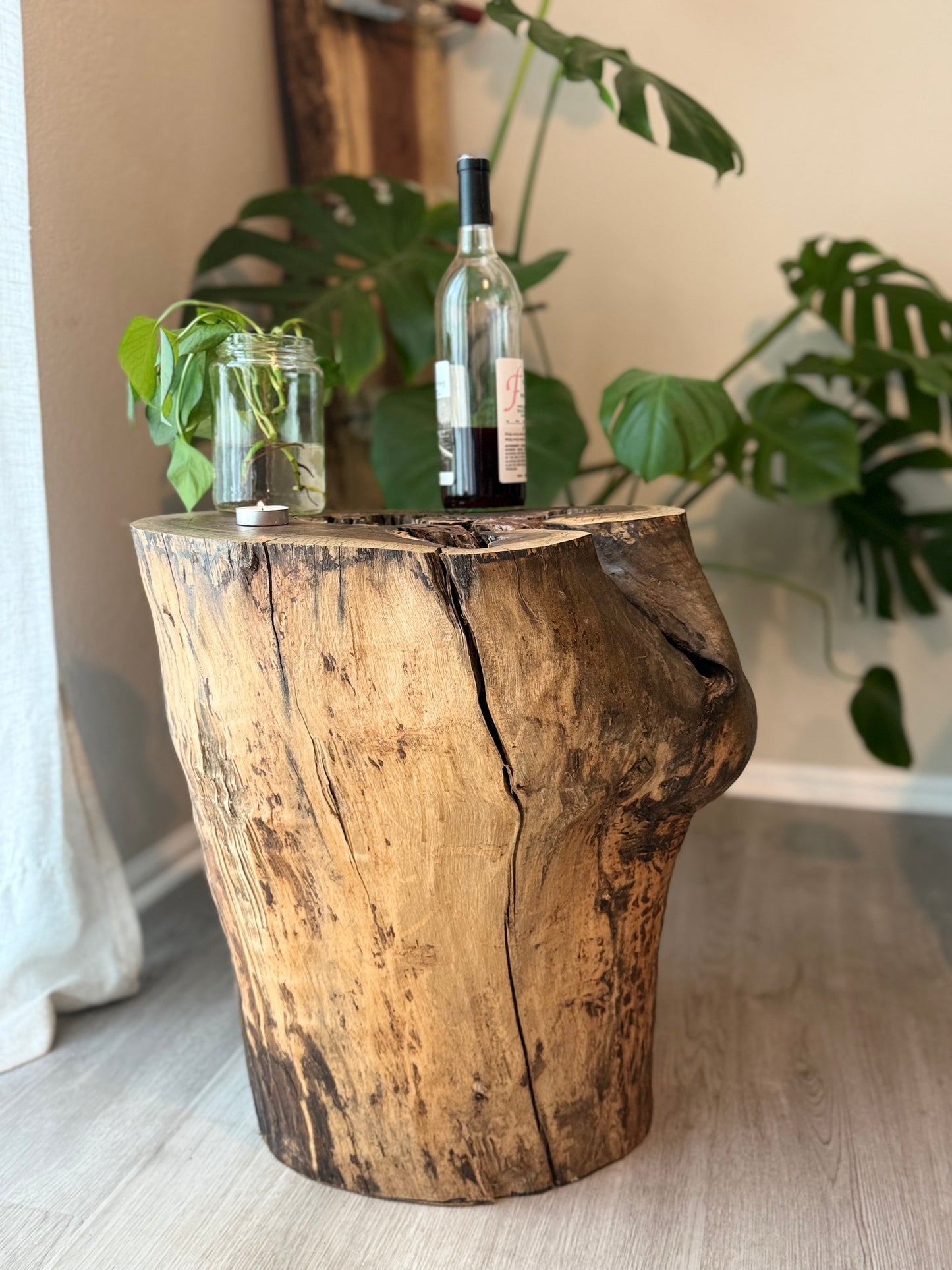 Wooden log side table with a bottle and greenery on a light-colored floor.