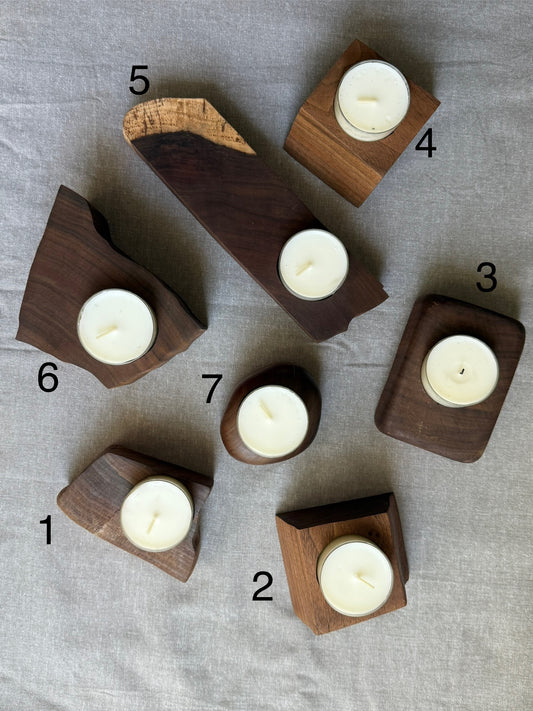 Seven numbered walnut candle holders arranged on linen backdrop – each with a white tea light candle, showcasing unique shapes.