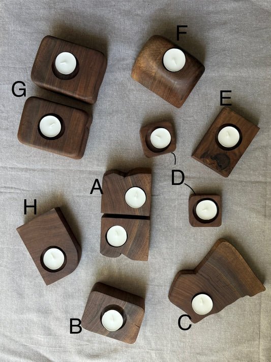 Eight lettered walnut candle holders arranged on linen backdrop – each with a white tea light candle, showcasing unique shapes