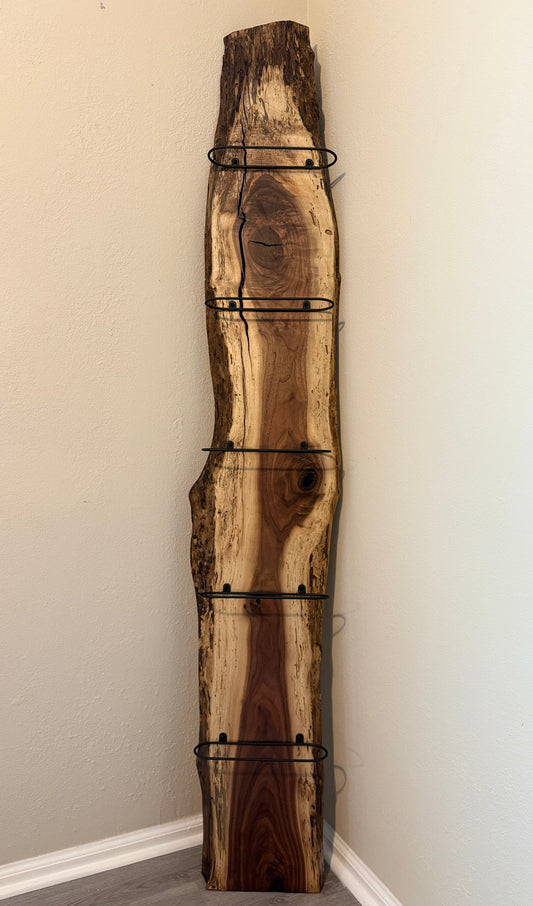 Vertical live edge walnut wine rack with black metal bottle holders.