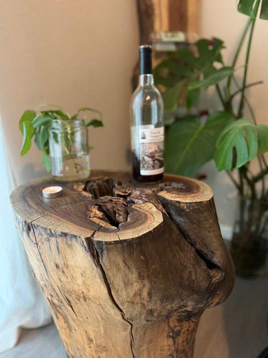Top profile of natural walnut stump staged with wine bottle, greenery, in ambient lighting to show rich grain patterns and natural cracks.